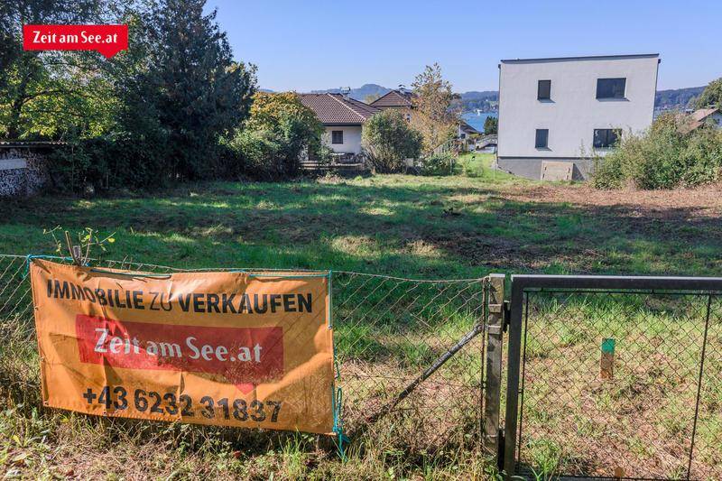 Unbebautes Grundstück mit einem "Immobilie zu verkaufen"-Schild, umgeben von Häusern und mit Seeblick.