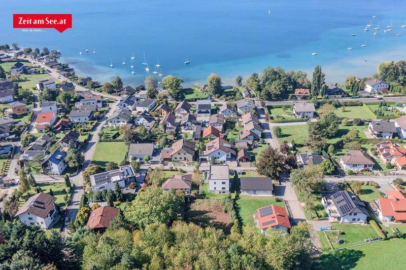 Weitläufige Luftaufnahme einer Wohngegend direkt am See mit zahlreichen Häusern und üppiger Vegetation.