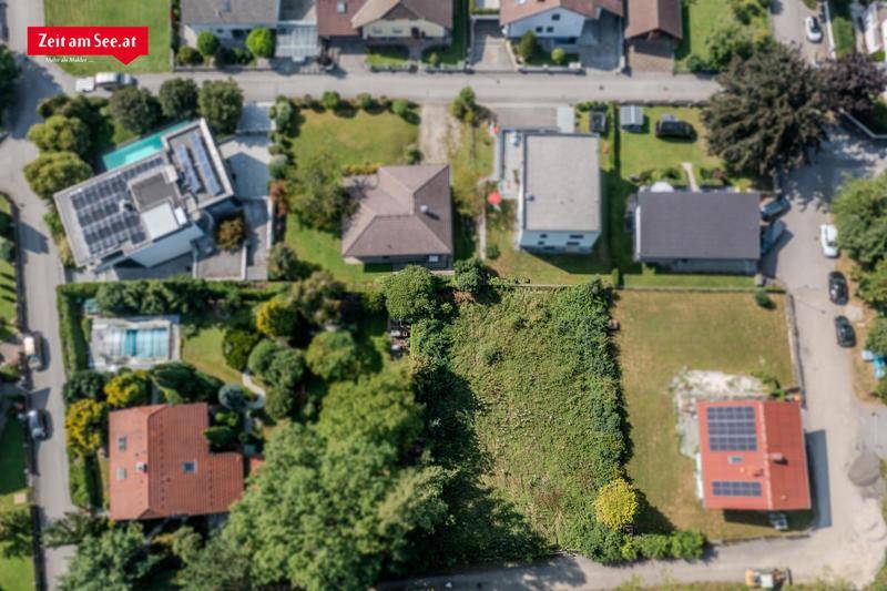 Vogelperspektive eines grünen Grundstücks umgeben von Wohnhäusern, einige mit Solaranlagen und Pool.