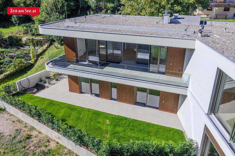 Draufsicht auf die moderne Villa mit Flachdach, Balkonen und umliegender grüner Landschaft.