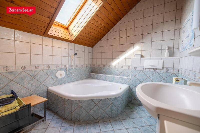 Badezimmer im Dachgeschoss mit Eckbadewanne, Dachfenster und blauen Fliesen.