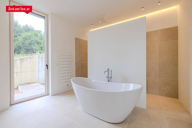 Modernes Badezimmer mit freistehender Badewanne, großen Fliesen und Zugang nach draußen.