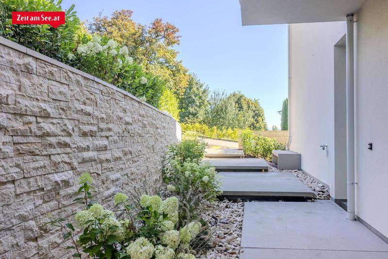 Steinmauer und moderne Betonstufen führen durch eine bepflanzte Außenanlage.