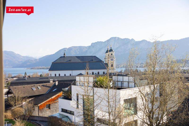 Panoramablick auf die Stadt, den See und die umliegenden Berge mit Kirche im Vordergrund.