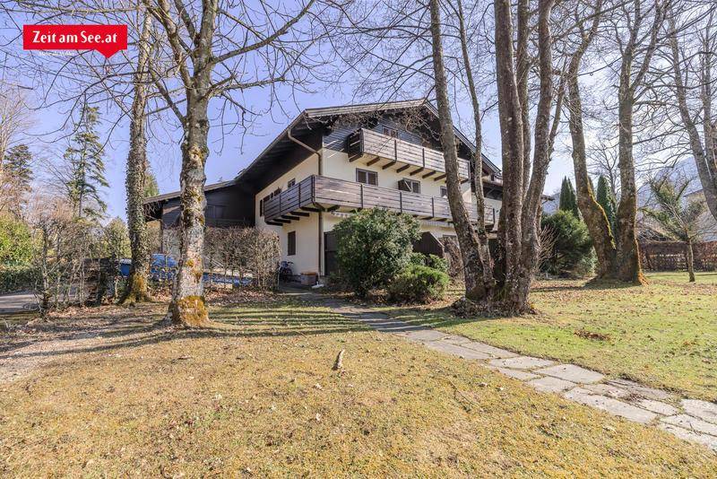 Traditionelles Haus mit Balkonen und einem gepflegten Vorgarten, umgeben von Bäumen in ländlicher Umgebung.