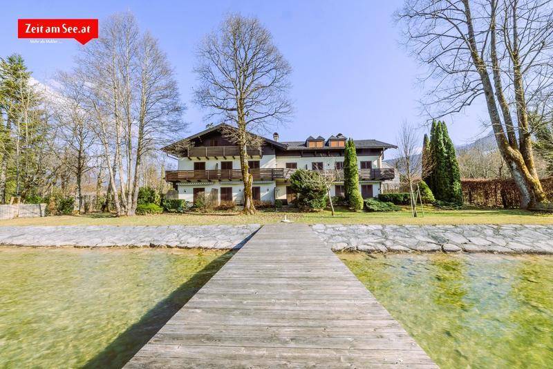 Traditionelles Gebäude am Seeufer mit großem Rasen, hohen Bäumen und einem langen Holzsteg, der in den See ragt.