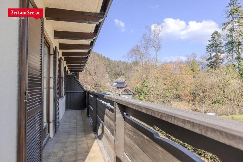 Langer Balkon mit Holzboden und Geländer, der einen Blick auf bewaldete Hügel und Berge bietet.