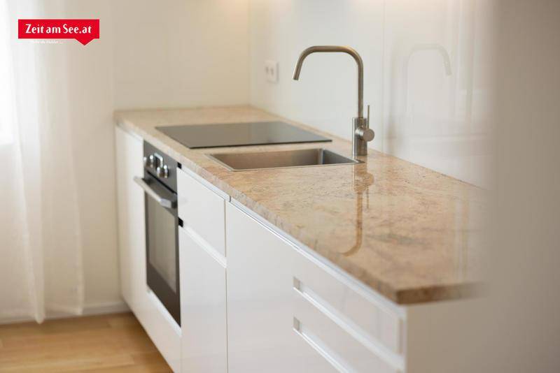 Moderne Küchenzeile mit heller Granit-Arbeitsplatte, integriertem Kochfeld, Spüle und Backofen.
