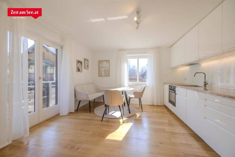 Offener Wohn- und Essbereich mit integrierter Küchenzeile, Holzboden und Zugang zu einem Balkon.