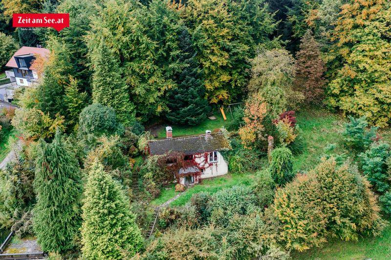 Luftaufnahme eines Hauses inmitten eines dicht bewachsenen Gartens mit Spielplatz und Waldrand.