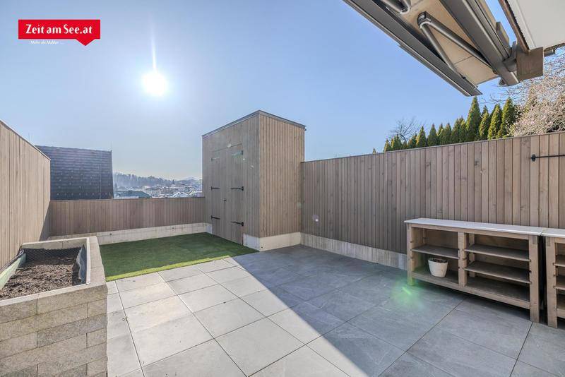 Sonniger Terrassenbereich mit Kunstrasen, Holzverkleidung und Außenmöbeln.