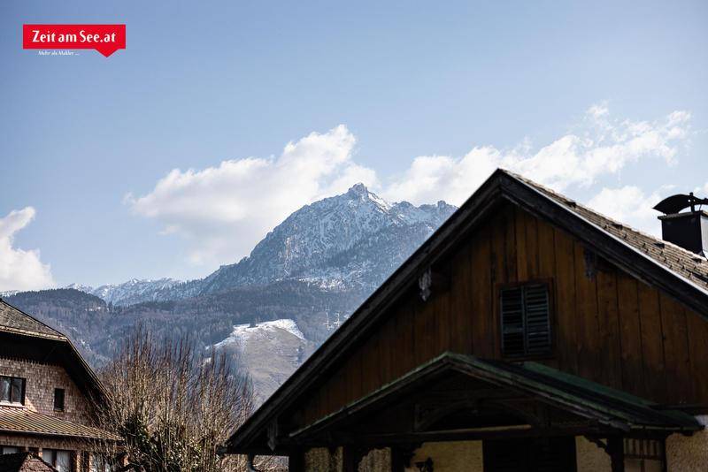 Traditionelles Hausdach mit Holzelementen vor einer beeindruckenden, schneebedeckten Bergkulisse.