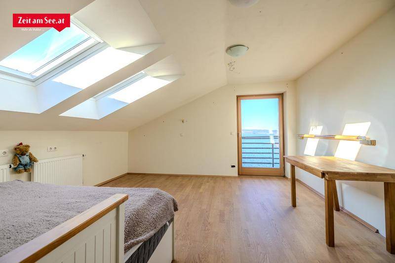 Helles Schlafzimmer im Dachgeschoss mit schrägen Wänden, Dachfenstern und Zugang zu einem Balkon mit Seeblick.