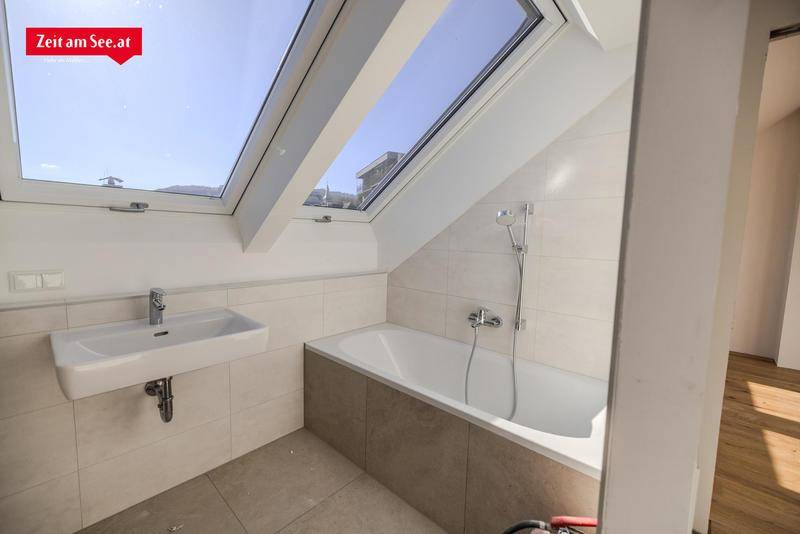 Modernes Badezimmer im Dachgeschoss mit Badewanne, Waschbecken und Dachfenster für Tageslicht.