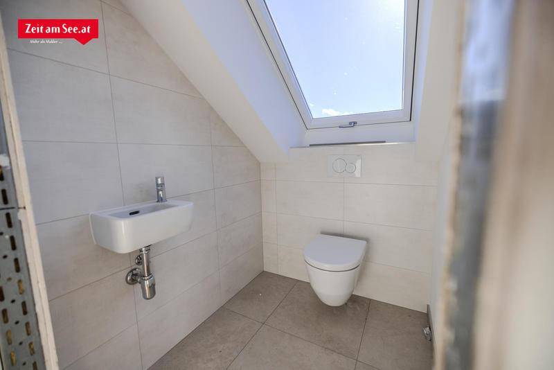 Separates WC mit wandmontierter Toilette, kleinem Waschbecken und Dachfenster.