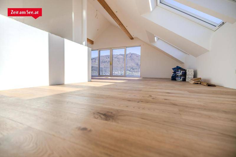 Geräumiger, heller Wohnbereich im Dachgeschoss mit Holzbalken, Parkettboden und großen Fenstern.