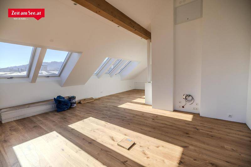 Lichtdurchfluteter Dachgeschossraum mit Holzbalken, Parkettboden und mehreren Dachfenstern.