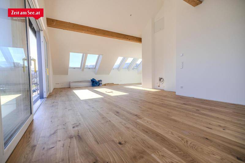 Heller Wohnbereich im Dachgeschoss mit Holzbalken, Parkettboden und Zugang zu einem Balkon.
