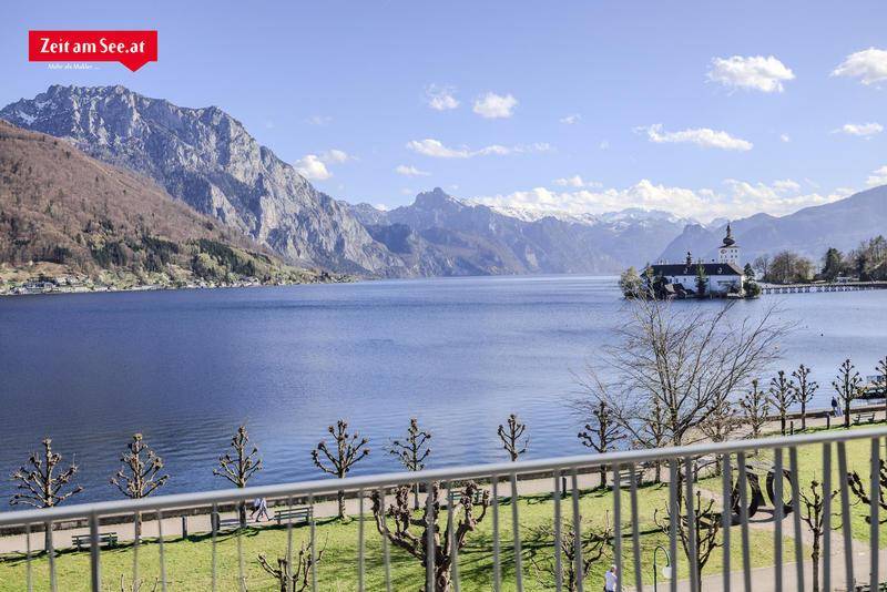 Atemberaubender Panoramablick vom Balkon auf den See, ein historisches Schloss und die majestätischen Berge.