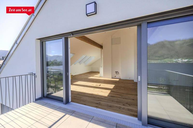 Heller Wohnraum im Dachgeschoss mit Holzbalken, Parkettboden und Zugang zu einem Balkon.