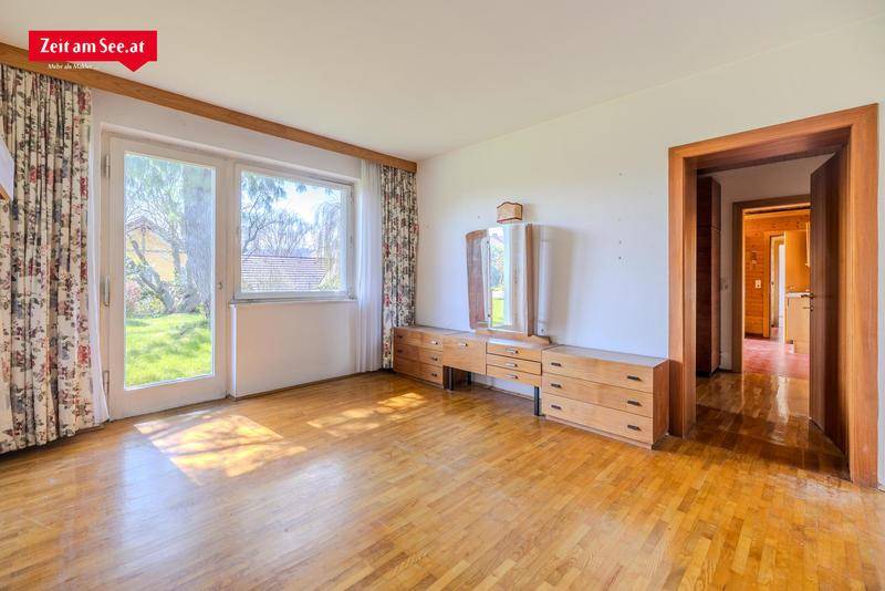 Geräumiges Schlafzimmer mit Holzkommode, Parkettboden und großem Fenster mit Zugang nach draußen.