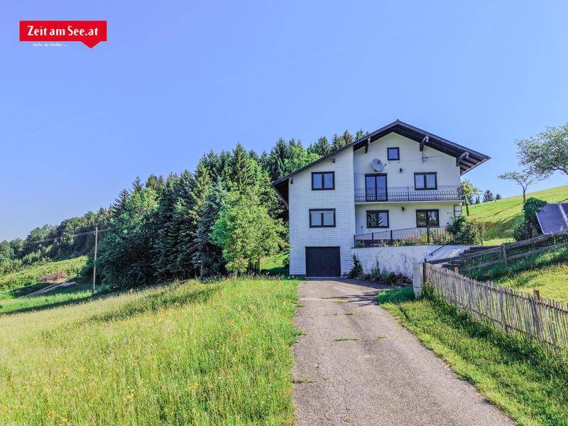 Vorderansicht des Hauses mit integrierter Garage und Zufahrt, umgeben von Grünflächen.