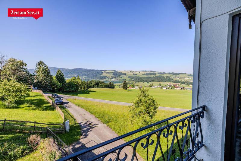 Blick vom Balkon auf die Straße, grüne Felder und den fernen See.