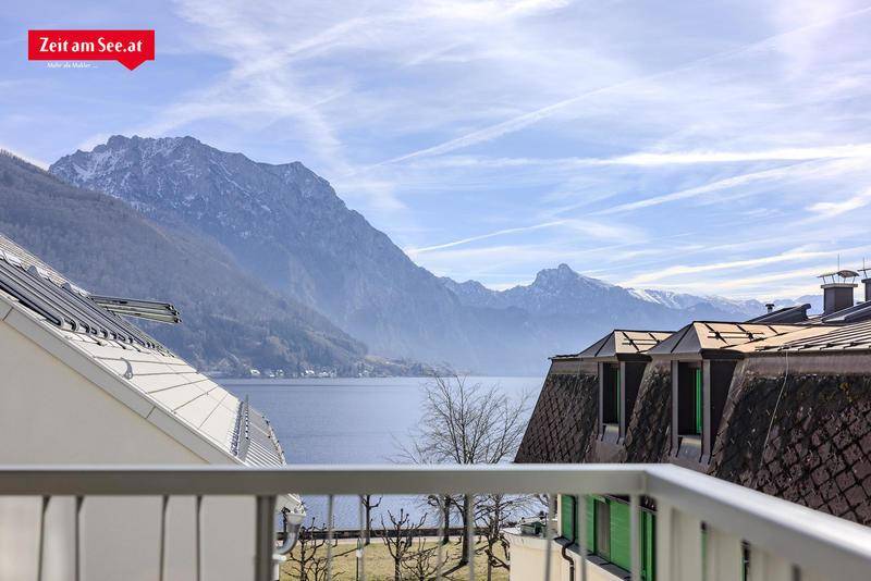 Panoramablick vom Balkon auf den See und die umliegenden Berge unter einem weiten Himmel.