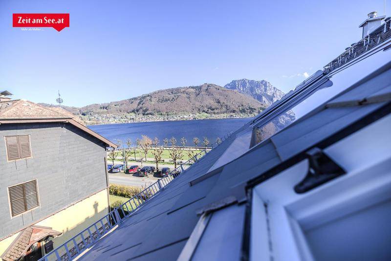 Blick über ein Dach mit Dachfenstern auf einen See und die beeindruckende Berglandschaft im Hintergrund.