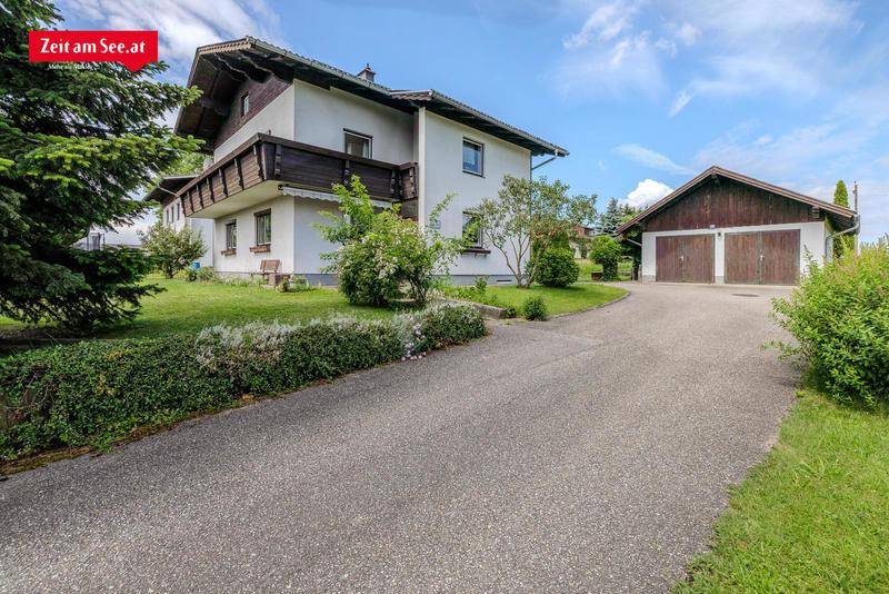 Zufahrt zum Haus mit Doppelgarage und gepflegtem Vorgarten unter blauem Himmel.