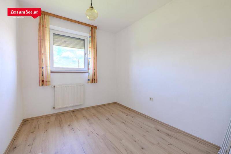 Leeres Zimmer mit Laminatboden und einem Fenster, das viel Tageslicht hereinlässt.