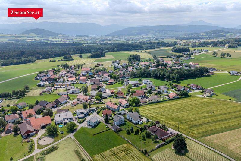 Weitläufige Luftaufnahme eines ländlichen Dorfes eingebettet in grüne Hügel und Felder.
