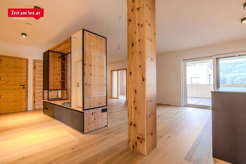 Offener Wohnbereich mit Holzelementen, einem Holzbalken und Zugang zu einem sonnigen Balkon.