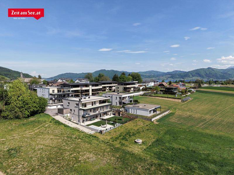 Weitläufige Luftaufnahme des Wohnkomplexes mit umliegenden Feldern und Bergen im Hintergrund.