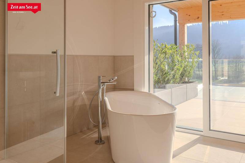Helles Badezimmer mit freistehender Badewanne und großem Fenster mit Zugang zur Terrasse.
