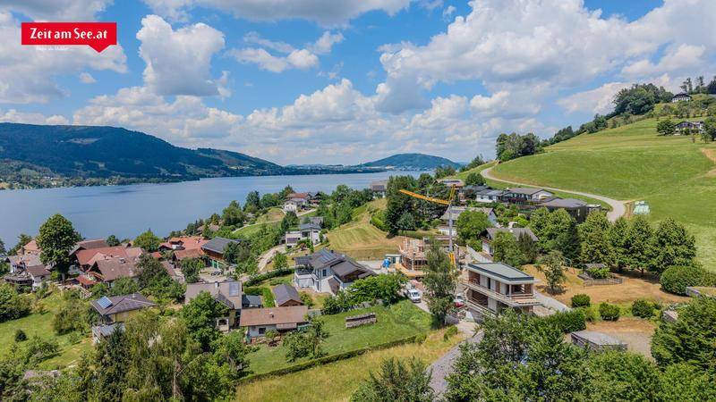 Weitläufige Luftaufnahme einer Wohnsiedlung am Seeufer mit umliegenden Hügeln und Neubauten im Bau.