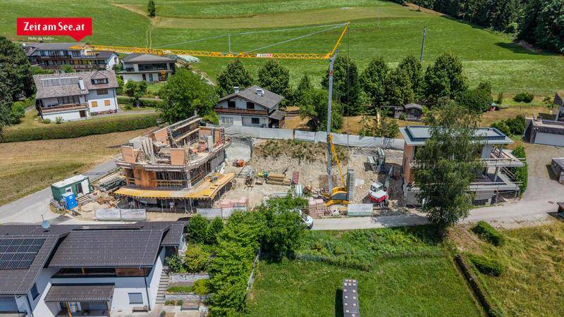Luftaufnahme einer Baustelle mit mehreren im Bau befindlichen Häusern inmitten grüner Felder und Bäume.
