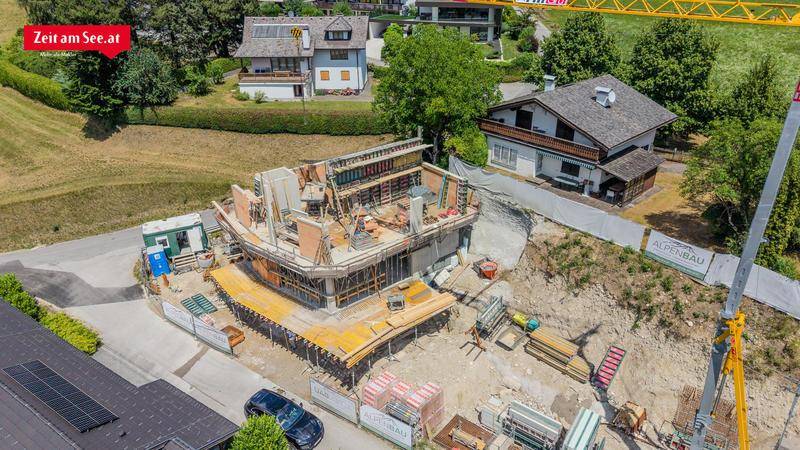 Luftaufnahme einer Baustelle für ein neues Wohngebäude, umgeben von bestehenden Häusern und Grünflächen.