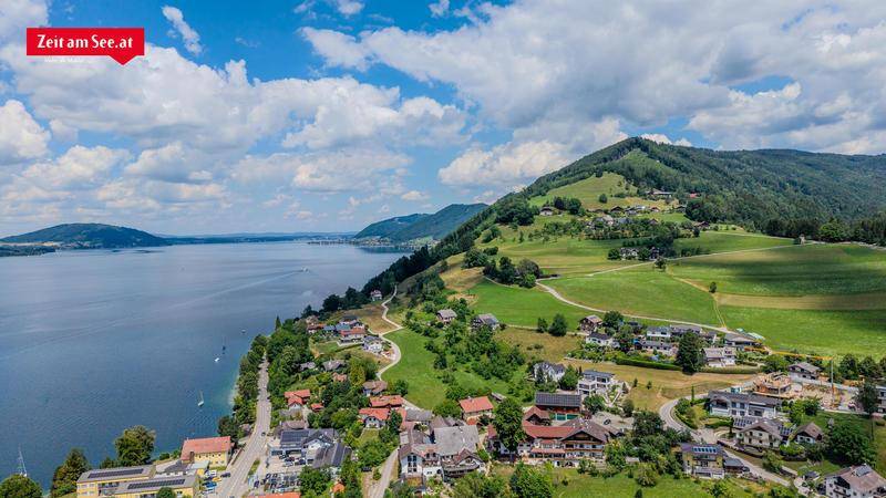Panoramablick auf eine idyllische Seenlandschaft mit grünen Hügeln und einer Siedlung am Ufer.