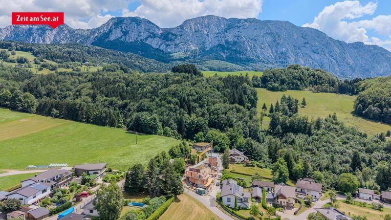 Weitläufige Landschaft mit grünen Wäldern, Wiesen und Bergen, umgeben von Wohnhäusern und einem Neubau.