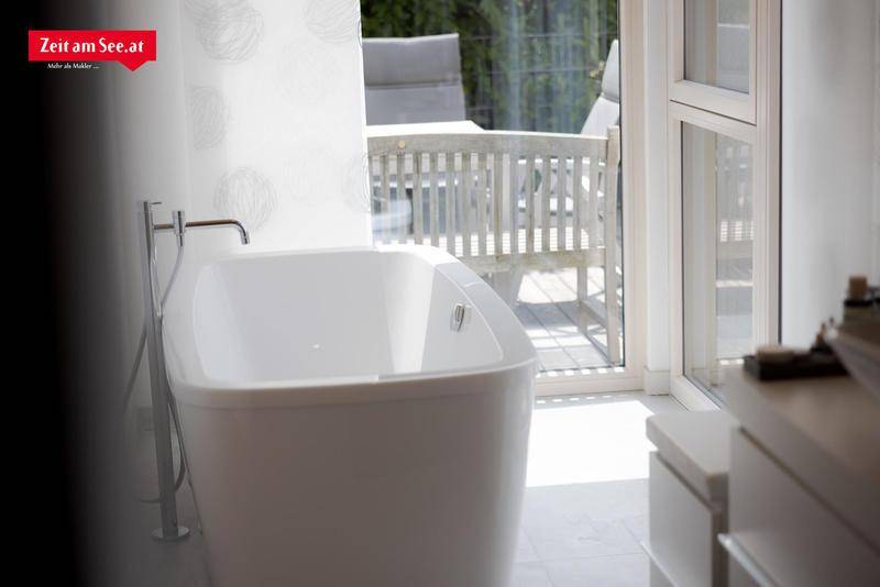 Freistehende Badewanne im hellen Badezimmer mit Blick auf die Terrasse und den Garten.