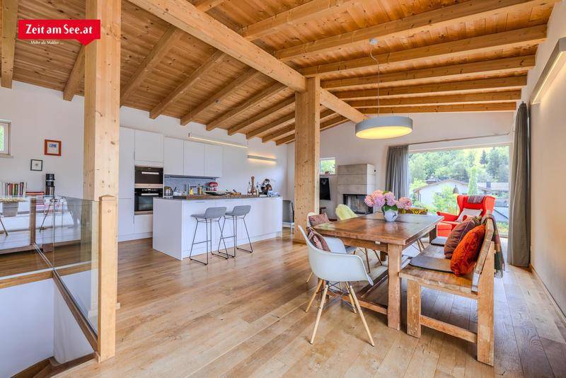 Offener Wohn-Essbereich mit moderner Küche, Holzbalkendecke und Zugang zur Terrasse mit Seeblick.