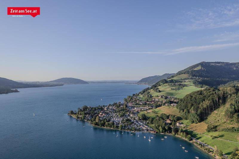 Malerische Luftaufnahme eines Sees mit umliegenden Bergen und einer Siedlung am Ufer.