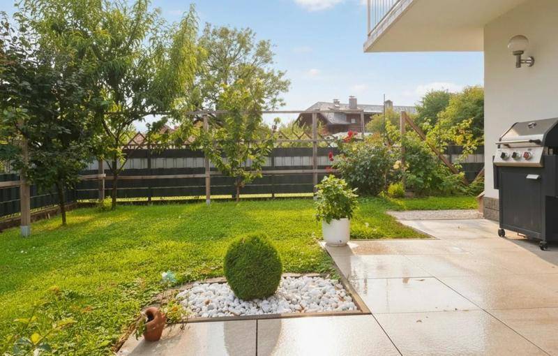Gepflegter Garten mit Rasenfläche, einer gepflasterten Terrasse und einem Grillbereich.