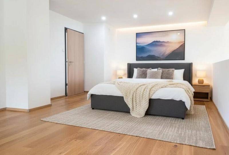 Modernes Schlafzimmer mit Doppelbett, Holzboden und indirekter Beleuchtung für eine angenehme Atmosphäre.