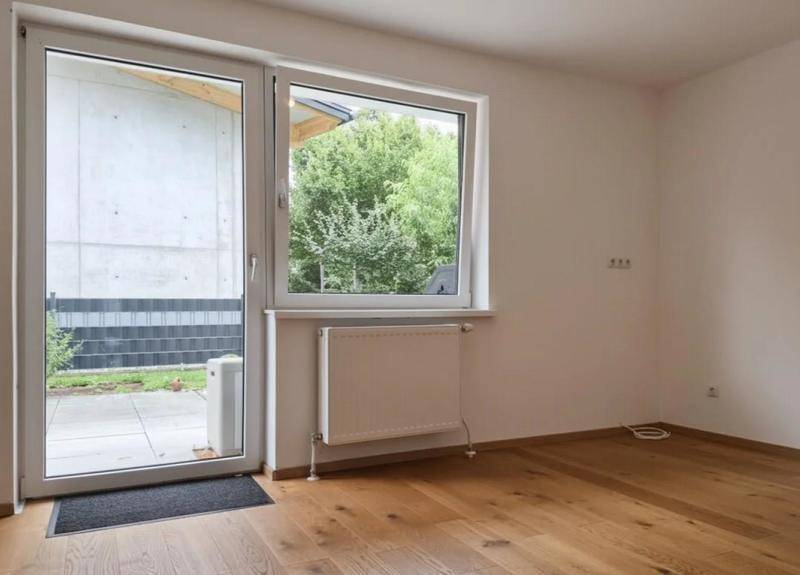 Heller Raum mit Holzboden, großem Fenster und direktem Zugang zum Gartenbereich.
