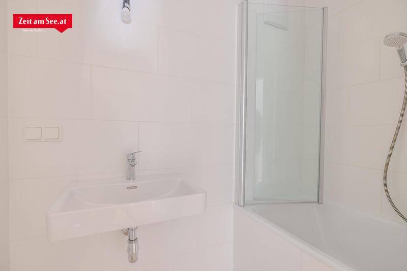 Modernes Badezimmer mit weißen Fliesen, einer Badewanne mit Duschabtrennung und einem einzelnen Waschbecken.
