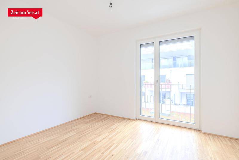 Leeres Schlafzimmer mit hellem Parkettboden und großem Fenster, das viel Tageslicht hereinlässt.
