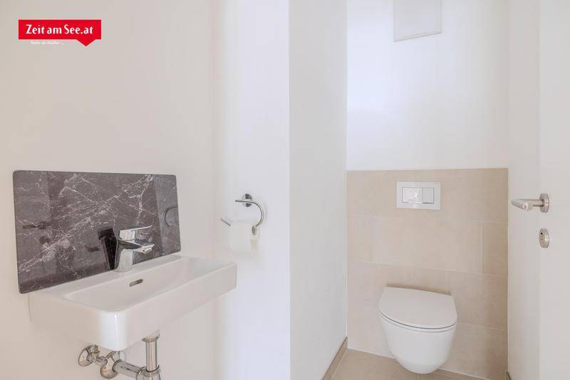 Modernes Gäste-WC mit wandhängender Toilette und kleinem Waschbecken mit dunkler Marmor-Rückwand.