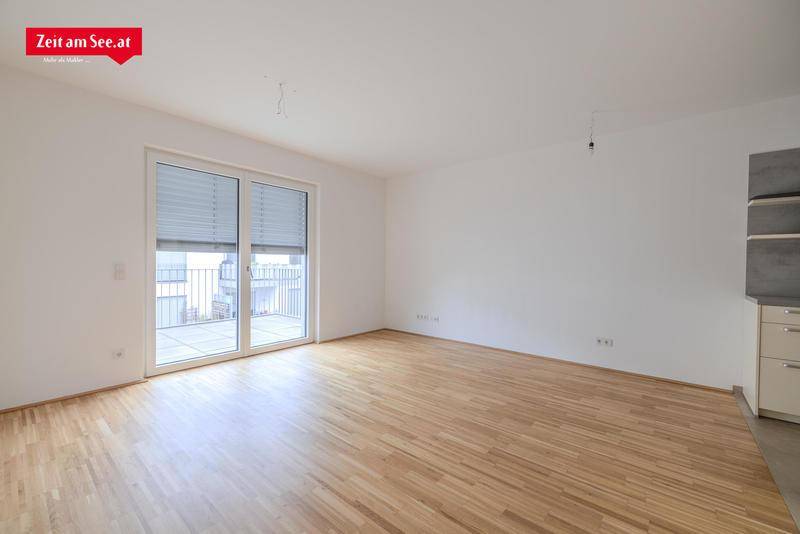 Heller Wohnbereich mit Parkettboden und großem Fenster, das Zugang zu einem Außenbereich bietet.